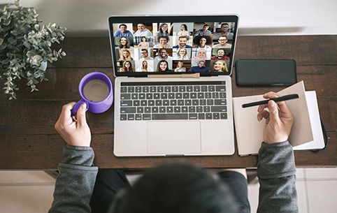 Person sitting in front of a laptop in an online meeting with many people on the screen.