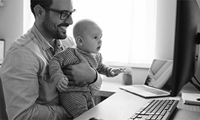 Man working on a computer while holding a baby in his lap